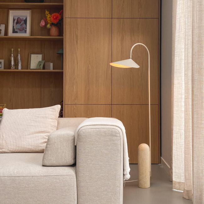 Een woonkamer met een bank van 4x6sofa en daarnaast een staande lamp 'Arum' van Ferm Living. Op de achtergrond een maatwerk wandkast van hout.